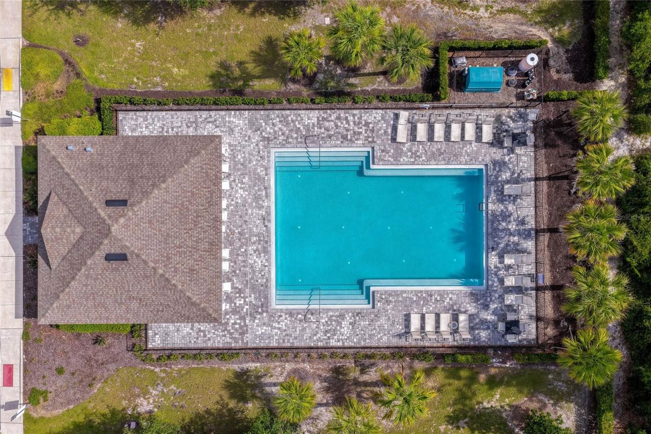 Photo 5 of 20: Overhead view of the pristine community pool area, featuring a large swimming pool, a spacious brick-paver sun deck, and tropical palm tree landscaping.