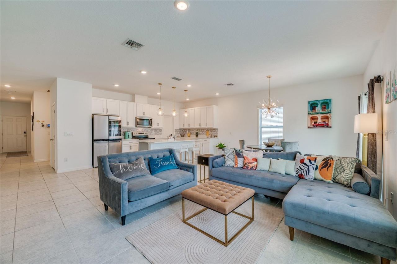 Photo 10 of 20: Generous open floor plan showing the continuous tiled flooring connecting the main living space directly to the kitchen area. A wide window and a sliding glass door offer views and access to the outdoors.