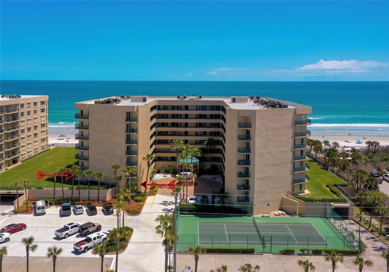 Photo 2 of 20: Elevated view highlighting the building’s main entrance, guest parking, and on-site tennis courts, all just moments from the beach.