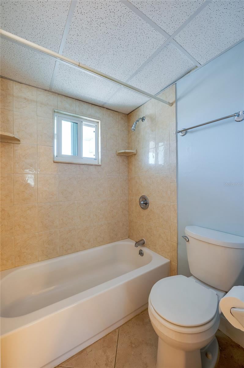 Photo 18 of 20: Full bathroom with a tiled tub and shower combination, complete with a window for natural light and ventilation.