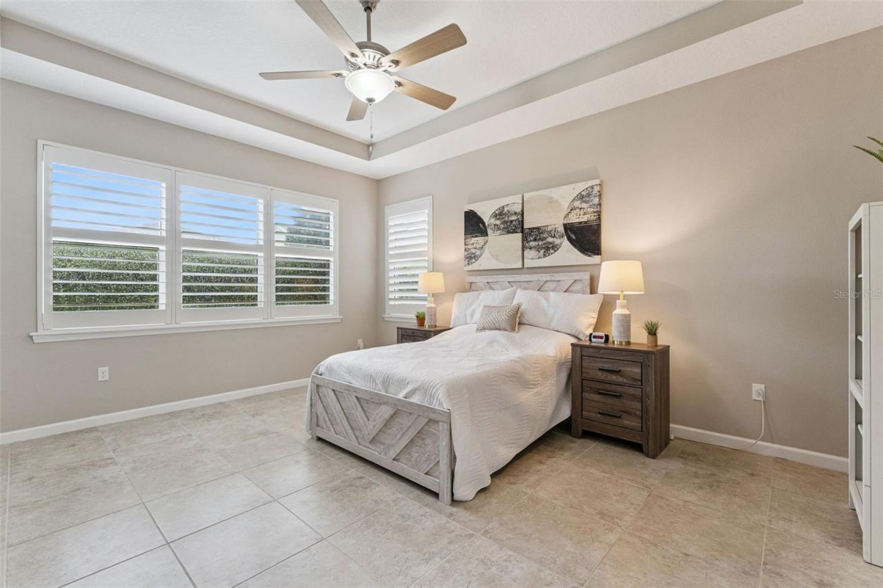 Photo 15 of 20: 14' x 17' Primary Bedroom w/ Plantation style shutters, tray ceiling, ceiling fan & ceramic tile floors