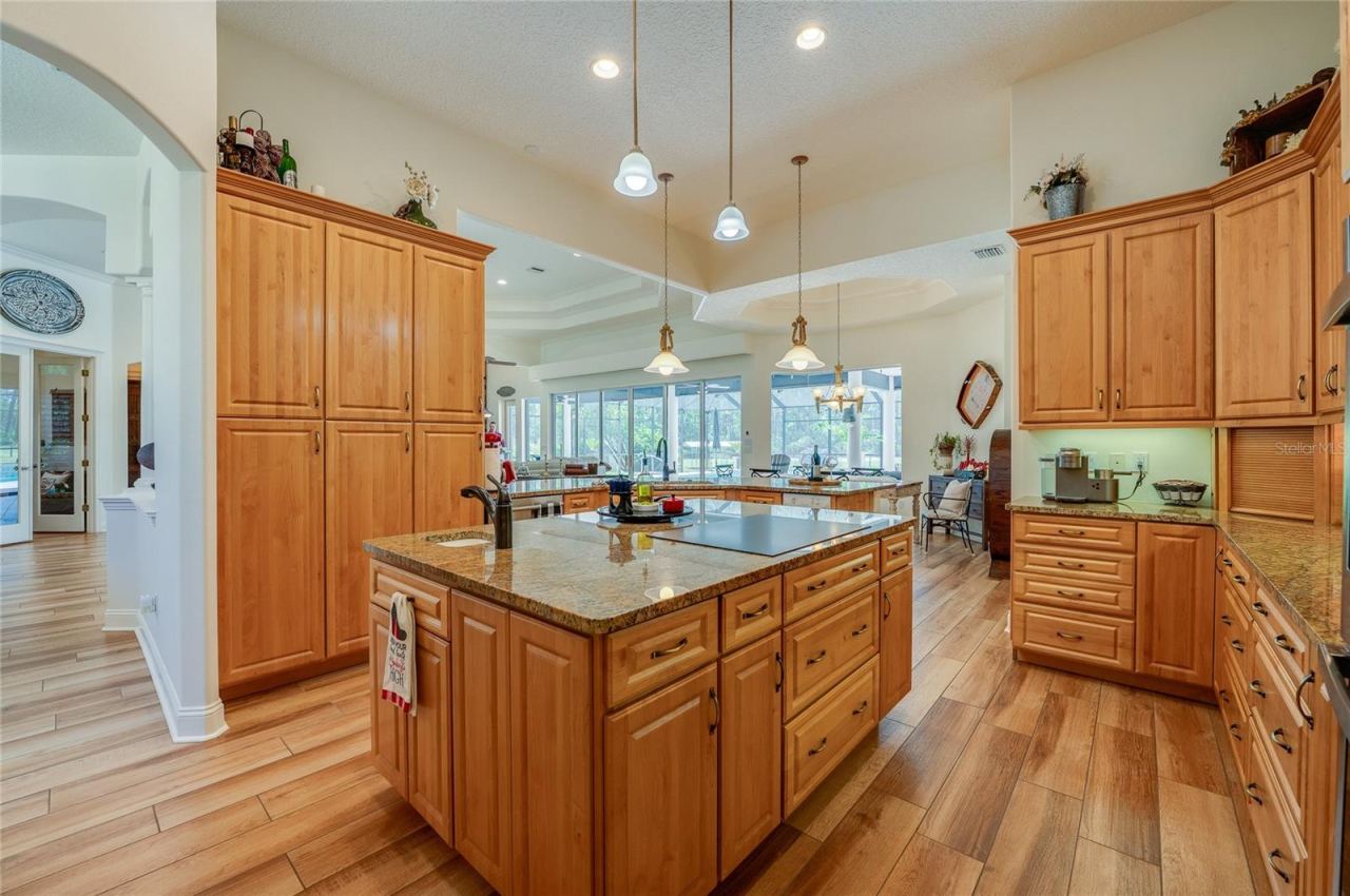 Photo 16 of 20: Expansive kitchen layout showcasing a massive granite-topped island with cooktop, prep sink, and surrounding tall storage cabinets.