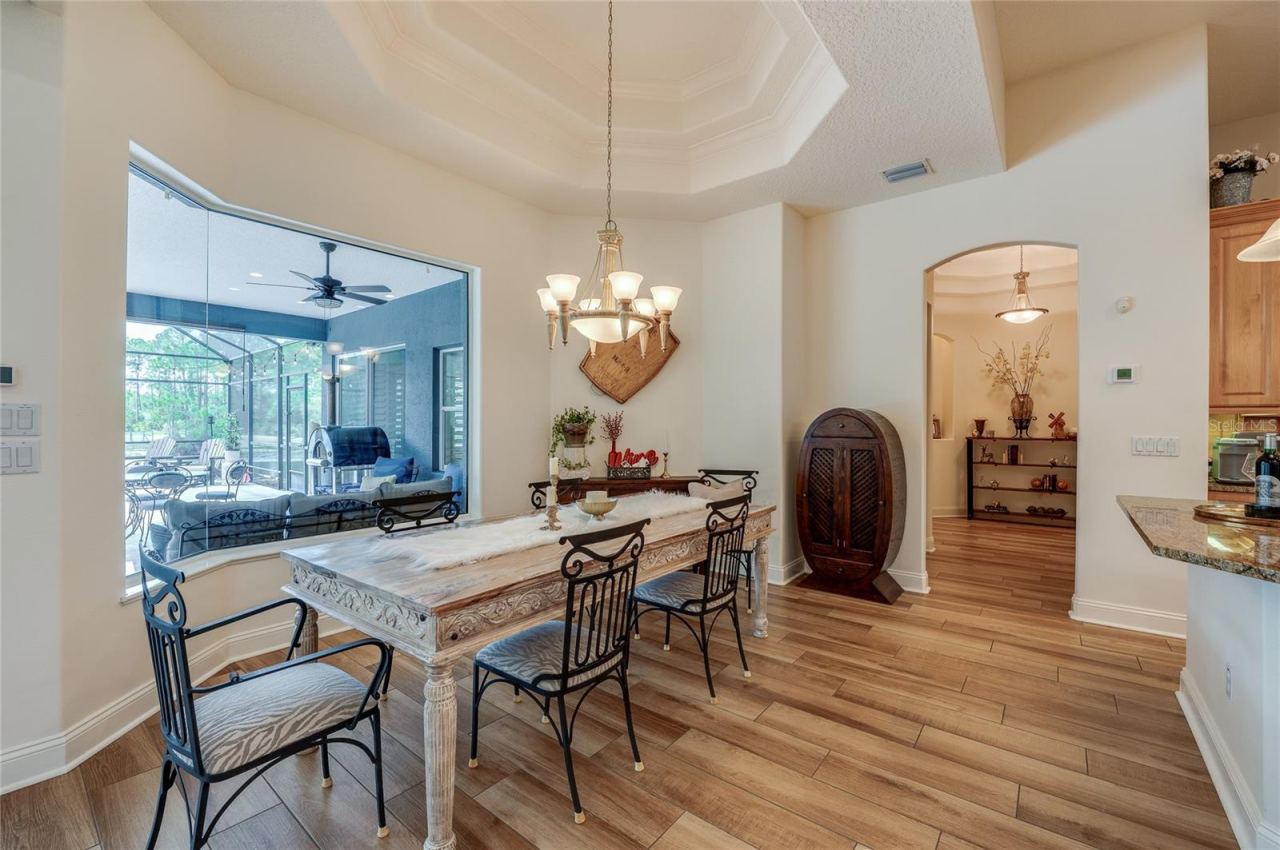 Photo 12 of 20: Bright dining nook featuring high recessed tray ceilings, a classic chandelier, and a large seamless picture window overlooking the outdoor patio area.