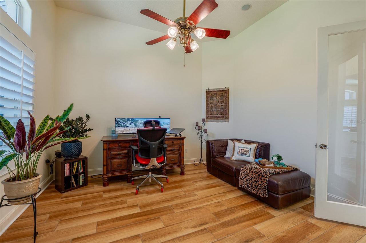 Photo 11 of 20: Dedicated home office setup with tile flooring, high ceilings, a ceiling fan, and plantation shutters.