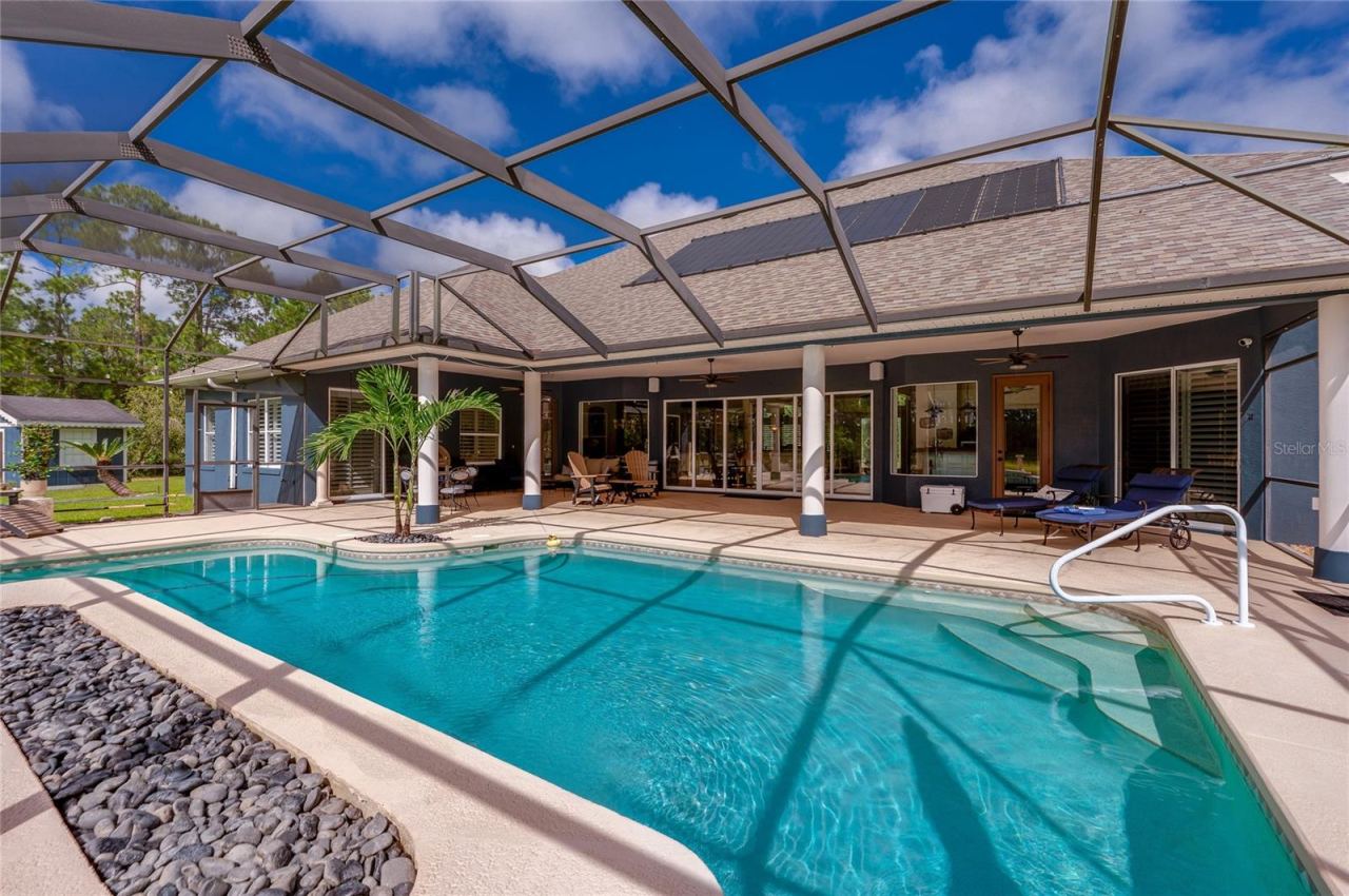 Photo 3 of 20: Overview of the screened pool enclosure showcasing roof-mounted solar panels and wide steps leading into the pool.