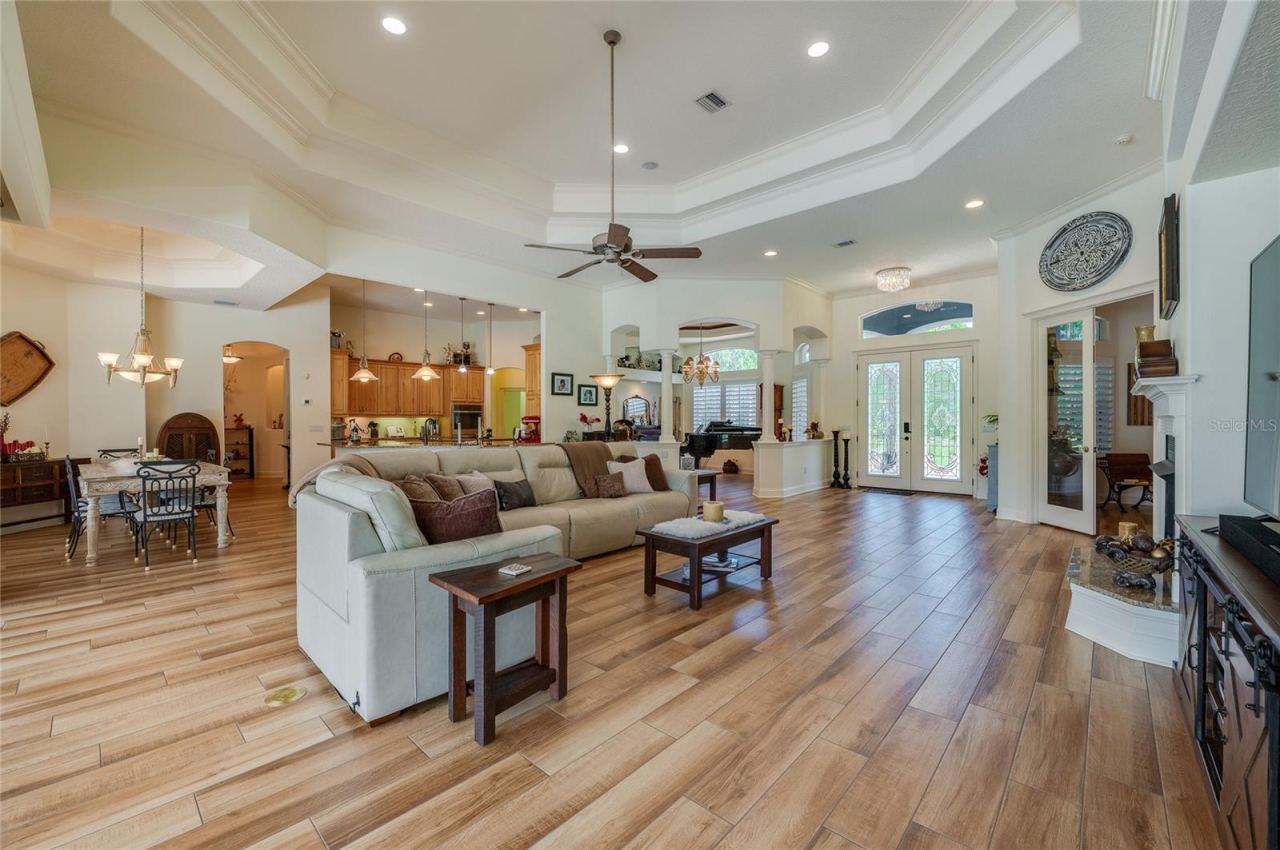 Photo 18 of 20: Sunlit main living room featuring high double-tray ceilings with a ceiling fan, tile flooring throughout, and immediate access to the entryway.