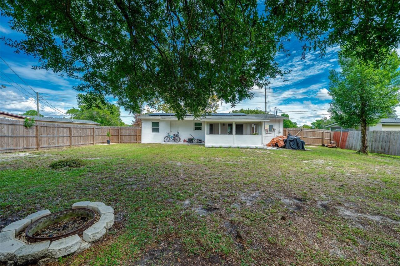 Photo 19 of 20: Generous rear lawn featuring a stone fire pit ring, full wood fencing, and direct views of the home's screened patio extension.
