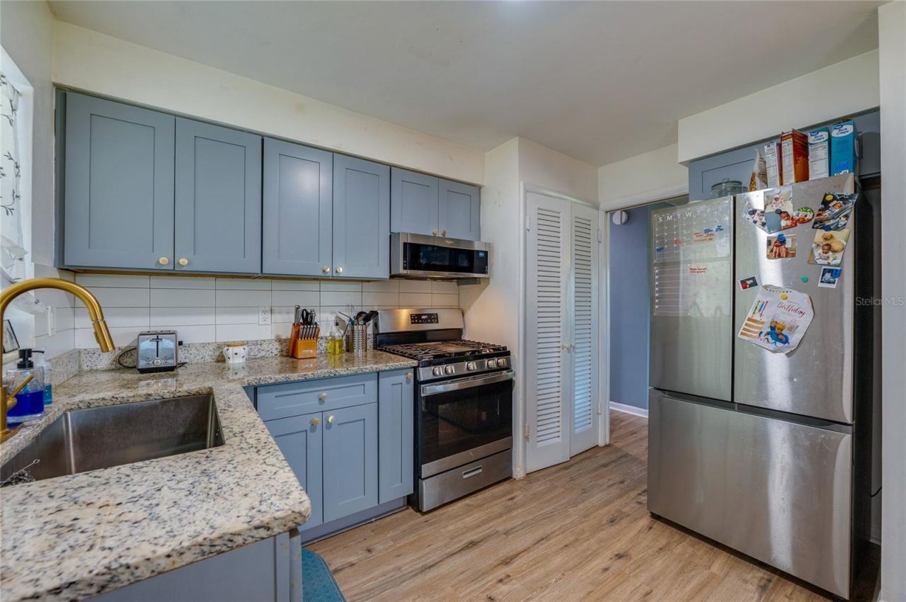 Photo 12 of 20: Modernized kitchen with stylish gray-blue cabinets, granite countertops, tile backsplash, and a large stainless steel refrigerator.