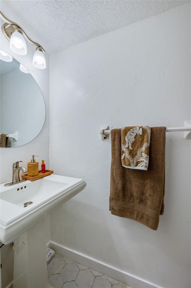 Photo 13 of 20: Compact half-bathroom with a white pedestal sink, rounded wall mirror, and modern lighting fixture.