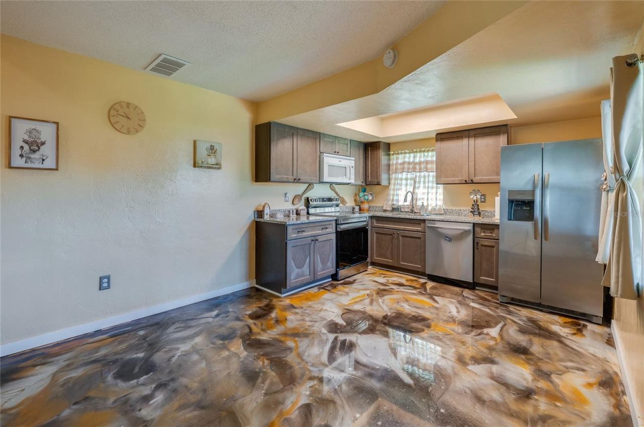 Photo 9 of 20: Functional kitchen equipped with stainless steel appliances, dark wooden cabinetry, granite countertops, and epoxy flooring.