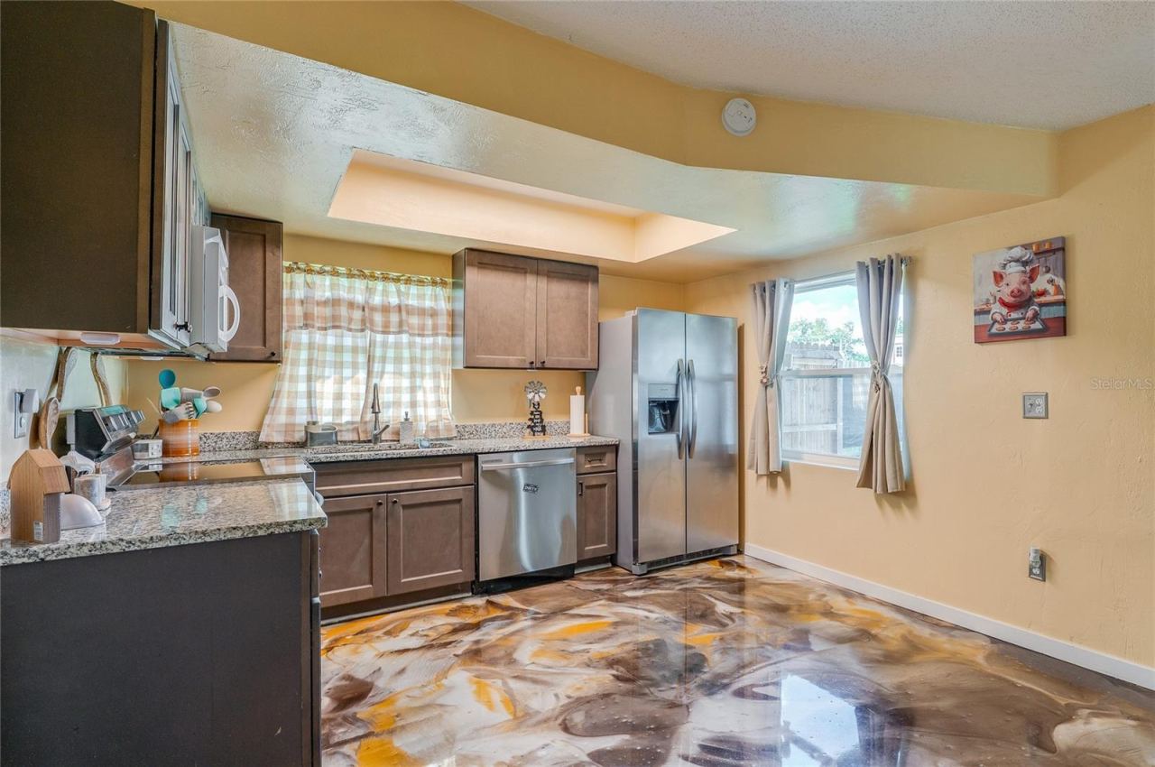 Photo 11 of 20: Functional kitchen space featuring stainless steel appliances, dark cabinetry, granite countertops, and eye-catching epoxy flooring.