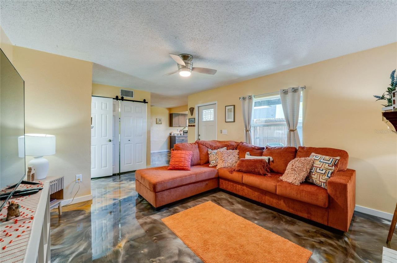 Photo 6 of 20: Bright living area featuring epoxy floors, a white front entrance door, and sliding closet doors leading to adjoining spaces.