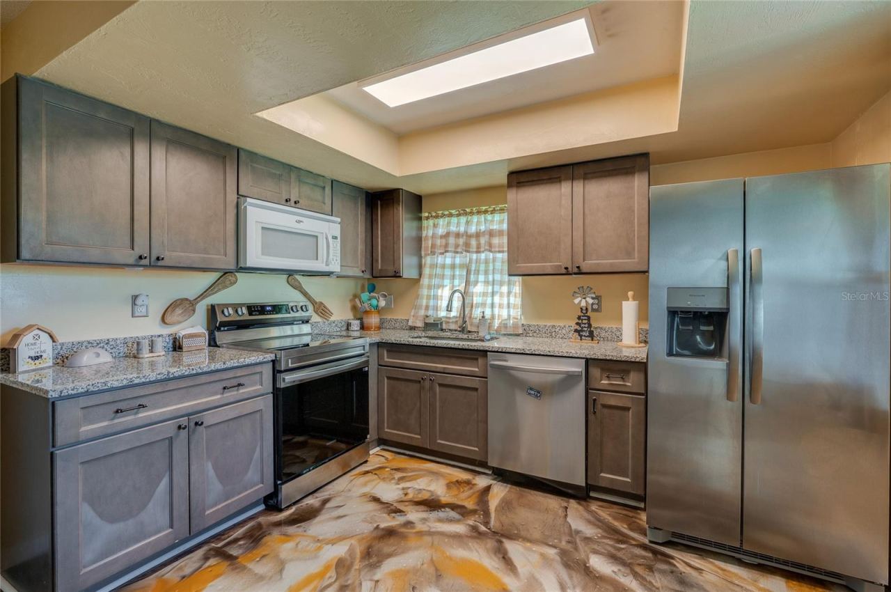 Photo 12 of 20: Upgraded kitchen area highlighting a full suite of stainless steel appliances, recessed ceiling light box, and custom epoxy flooring.