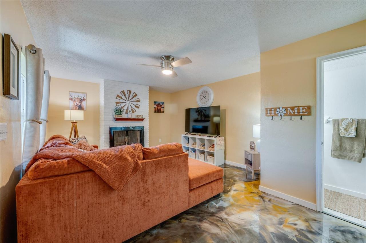 Photo 5 of 20: Spacious living area showcasing unique epoxy flooring, warm neutral walls, and a white brick accent wall with a fireplace.