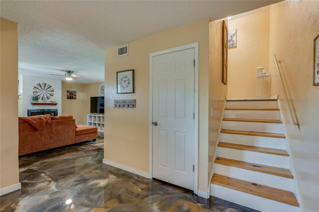 Photo 15 of 20: Foyer and entryway showing wooden stair steps with white risers, epoxy flooring, and access to an adjacent living area.