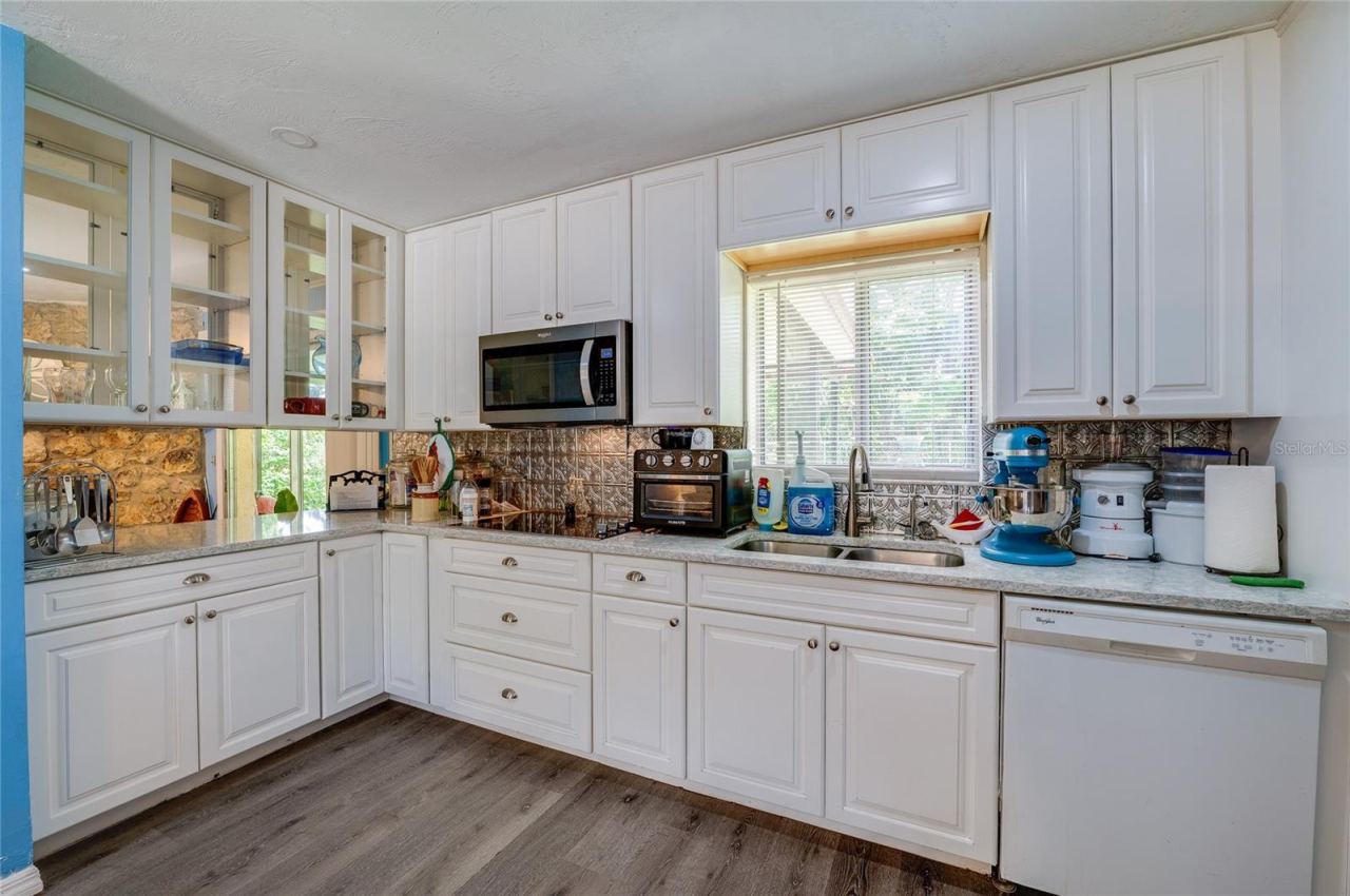 Photo 10 of 20: Functional kitchen layout complete with white cabinetry, glass-front upper cupboards, a double sink under a bright window, and built-in appliances.