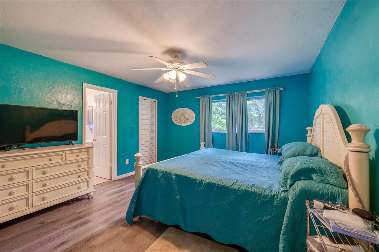 Photo 13 of 20: Primary bedroom suite styled with bright turquoise walls, LVP flooring, a white-panel closet, and direct access to an ensuite bathroom.