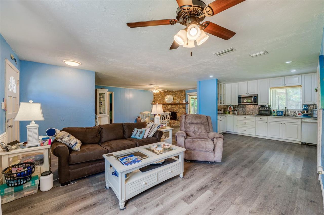 Photo 5 of 20: Bright open-concept living area with LVP flooring, cool blue walls, and a ceiling fan leading into the adjacent kitchen and dining spaces.