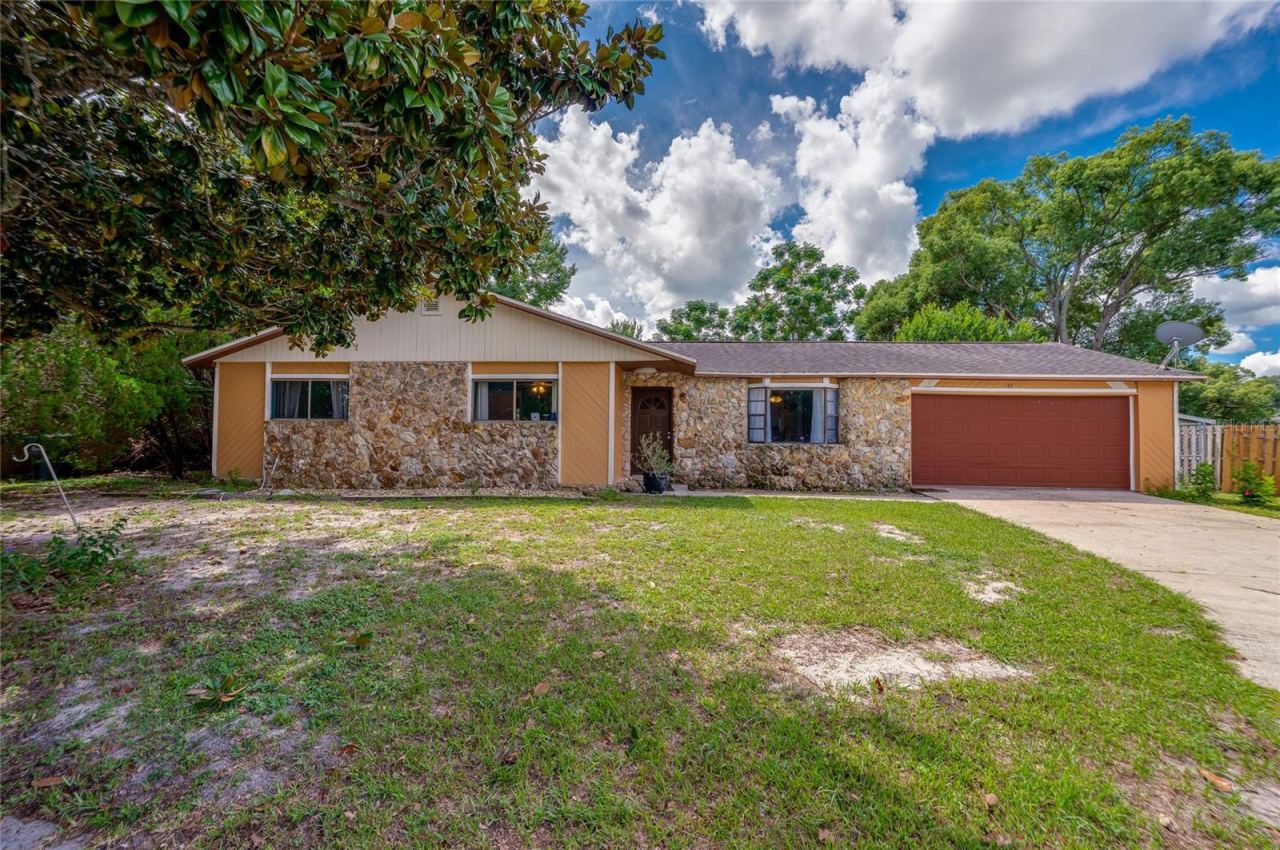 Photo 2 of 20: Front exterior of the ranch-style house showcasing decorative stone accent walls, a red garage door, concrete driveway, and front lawn.