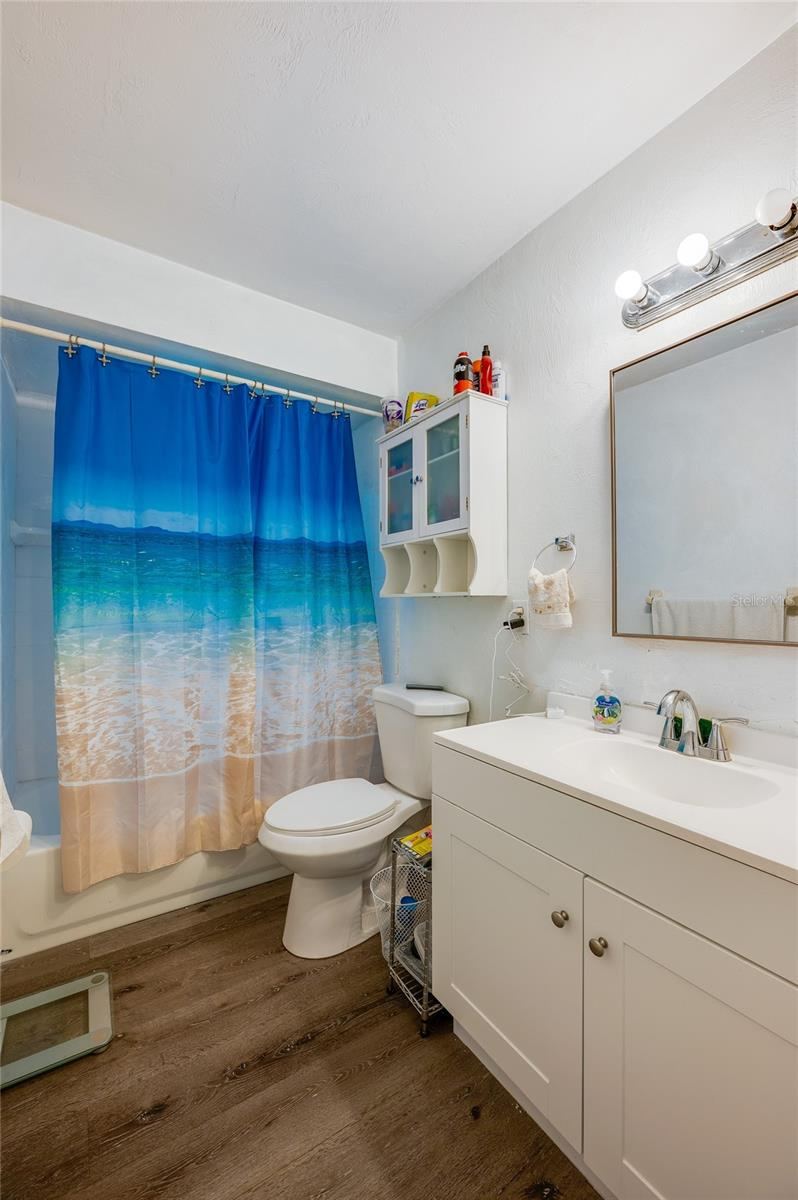 Photo 19 of 20: Full bathroom with a white vanity, mirrored medicine cabinet, and LVP flooring.
