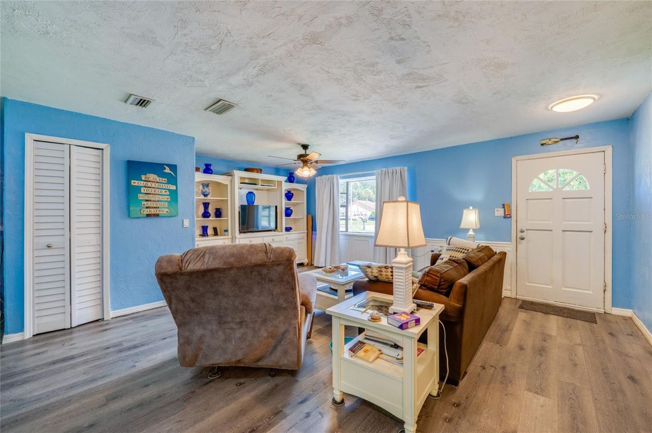 Photo 4 of 20: Open living space featuring light blue walls, LVP flooring, double closets, and a white front entry door with glass pane accents.