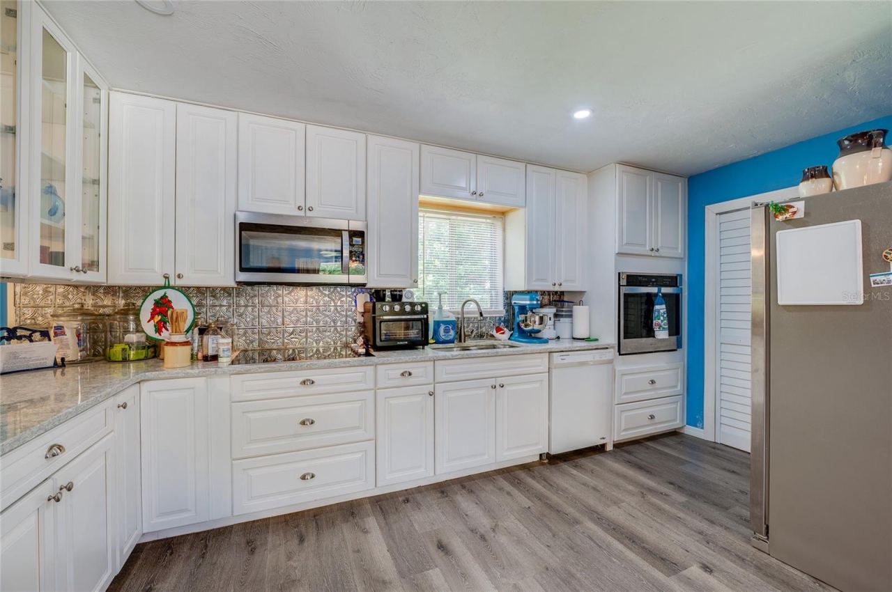 Photo 9 of 20: Well-equipped kitchen featuring crisp white cabinetry, textured tile backsplash, built-in appliances, and light grey LVP flooring.