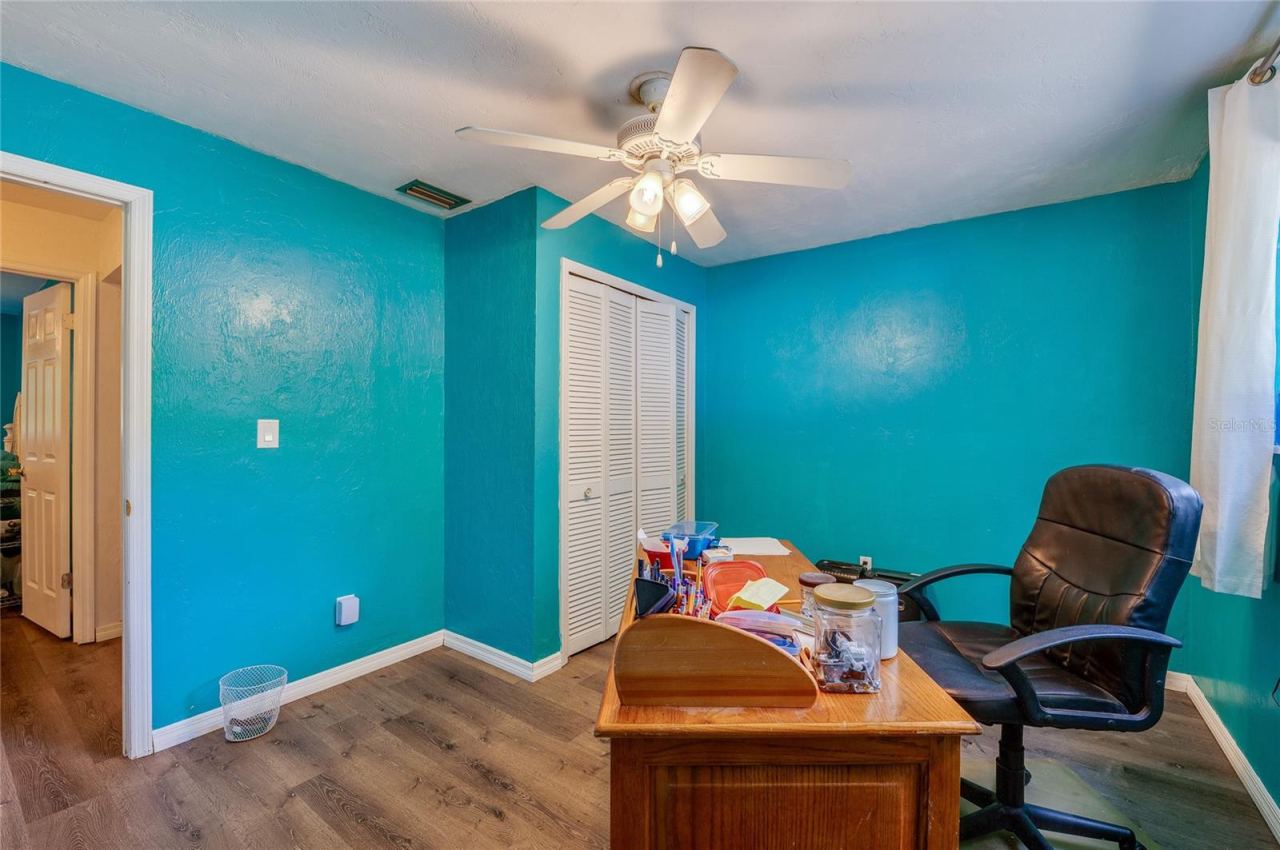 Photo 18 of 20: Functional home office/bedroom area illuminated by a ceiling fan, featuring turquoise walls, closet storage, and durable LVP flooring.