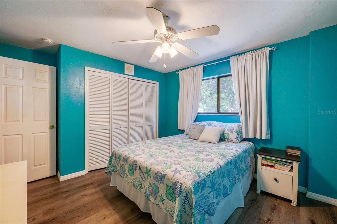 Photo 16 of 20: Bright bedroom showcasing vibrant blue walls, light-toned LVP flooring, and double louvered closet doors under a classic white ceiling fan.