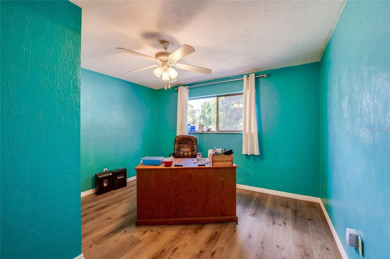Photo 17 of 20: Spacious home office/bedroom featuring vibrant teal walls, low-maintenance LVP flooring, and a large window providing ample natural light.