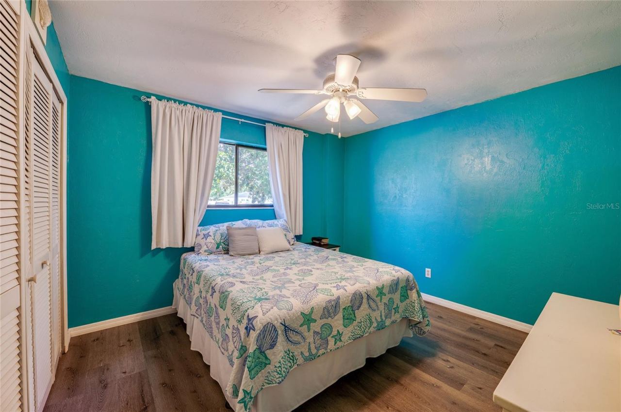 Photo 15 of 20: Vibrant coastal-themed bedroom accented with bright turquoise walls, modern LVP flooring, and a ceiling fan. Double closet doors offer ample storage space.