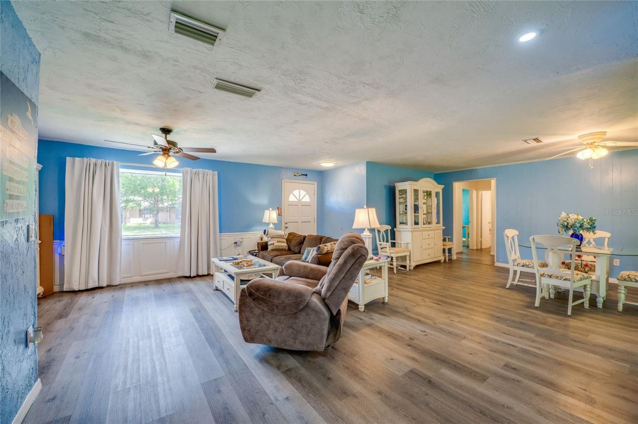 Photo 3 of 20: Spacious main living area displaying LVP flooring, light blue walls, a wide window bringing in natural light, and smooth transitions to adjoining rooms.