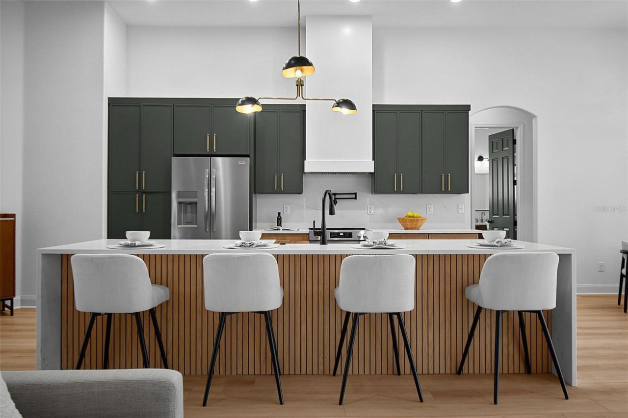 Photo 11 of 20: The kitchens centerpiece is the waterfall island in quartz countertop along with the sleek back wall featuring the beautiful tile backsplash, range, custom range hood along custom wood cabinets and quartz countertops.