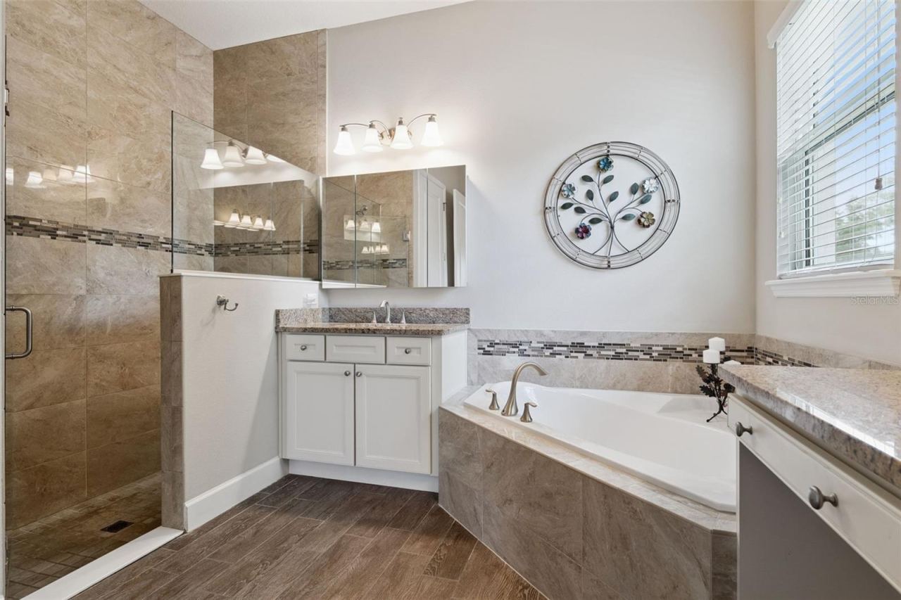 Photo 19 of 20: 12' x 11' Primary Bath w/ separate vanities, glass enclosed walk-in shower w/ bench seat & corner soaking tub
