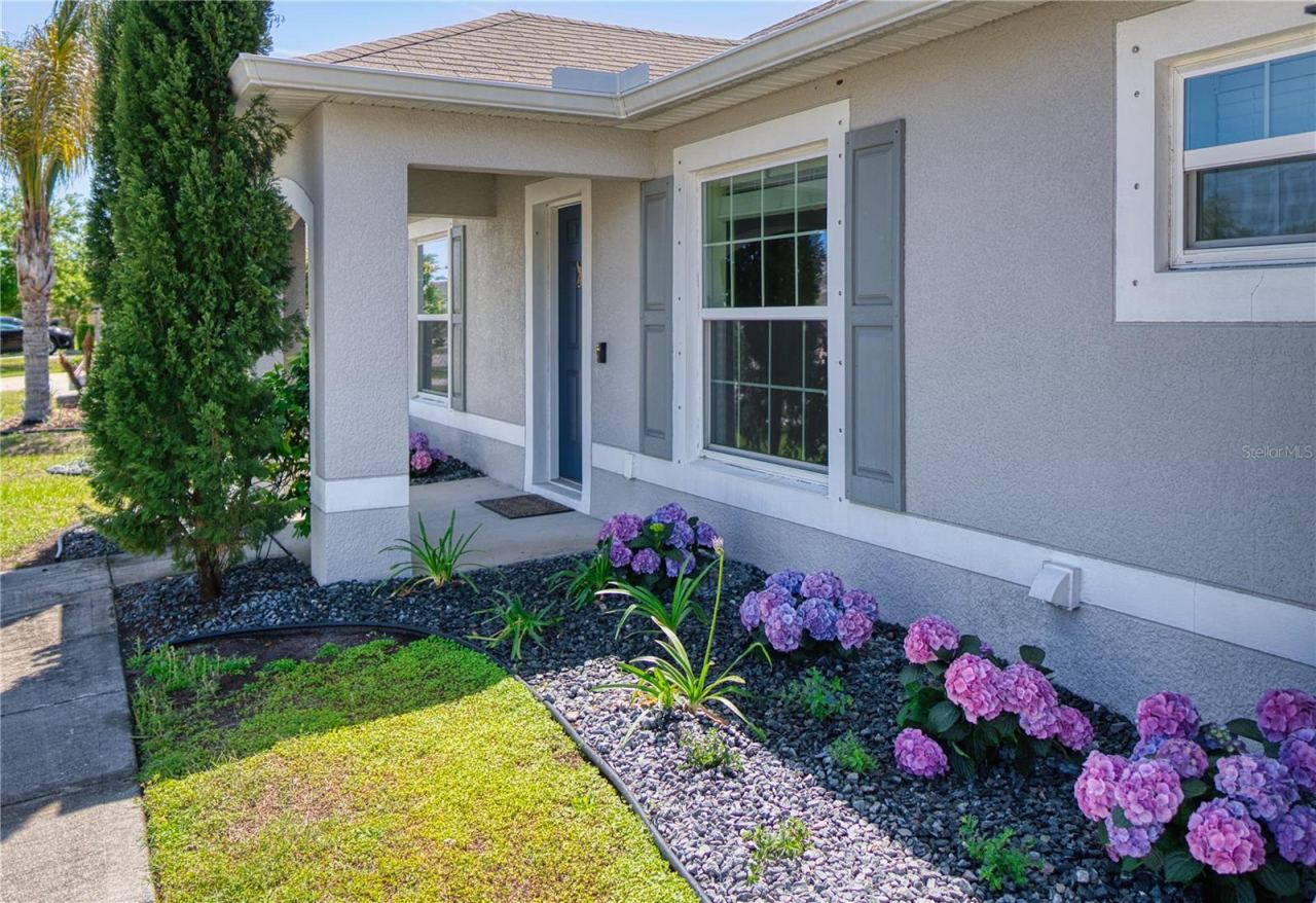 Photo 5 of 20: A graceful walkway leads to the covered front entrance, framed by attractive landscaping and colorful blooms that create a warm, welcoming approach.