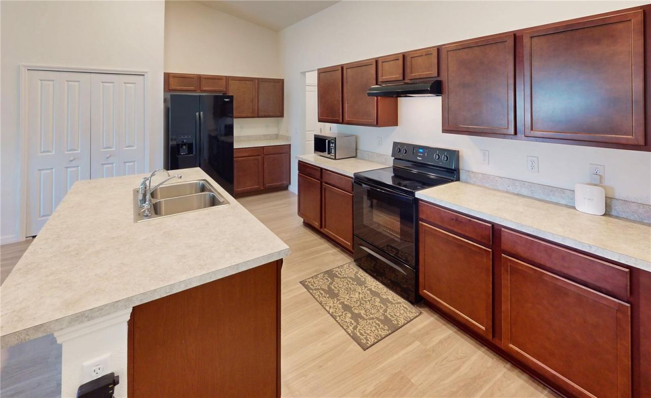 Photo 11 of 20: Rich wood cabinetry gives this kitchen a warm, upscale feel, with seven upper cabinets visible plus generous lower cabinetry and additional island storage, offering both beauty and function. The layout follows an efficient three-point kitchen design…