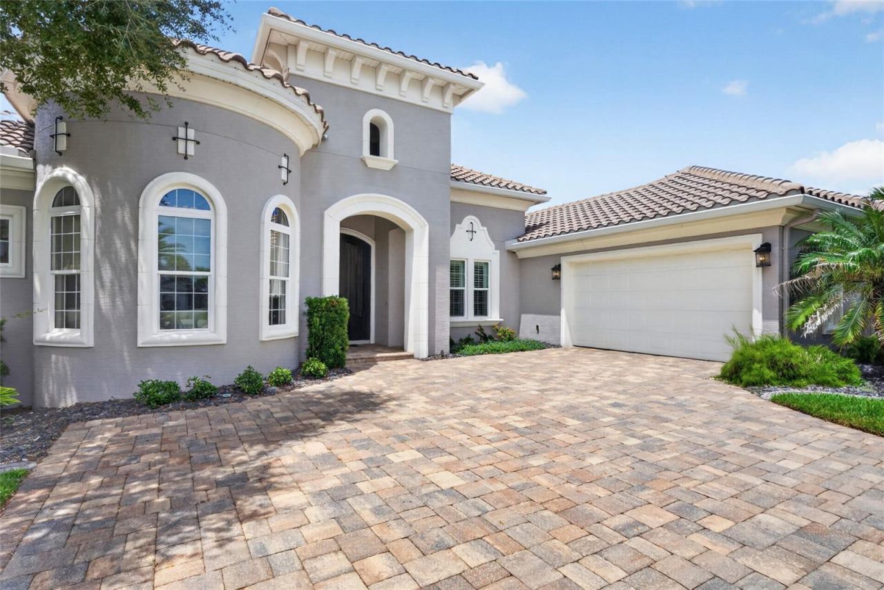 Photo 11 of 20: Step through the arched double doors where golden light spills across the paver drive, setting the tone for a home that welcomes you long before you reach the threshold.