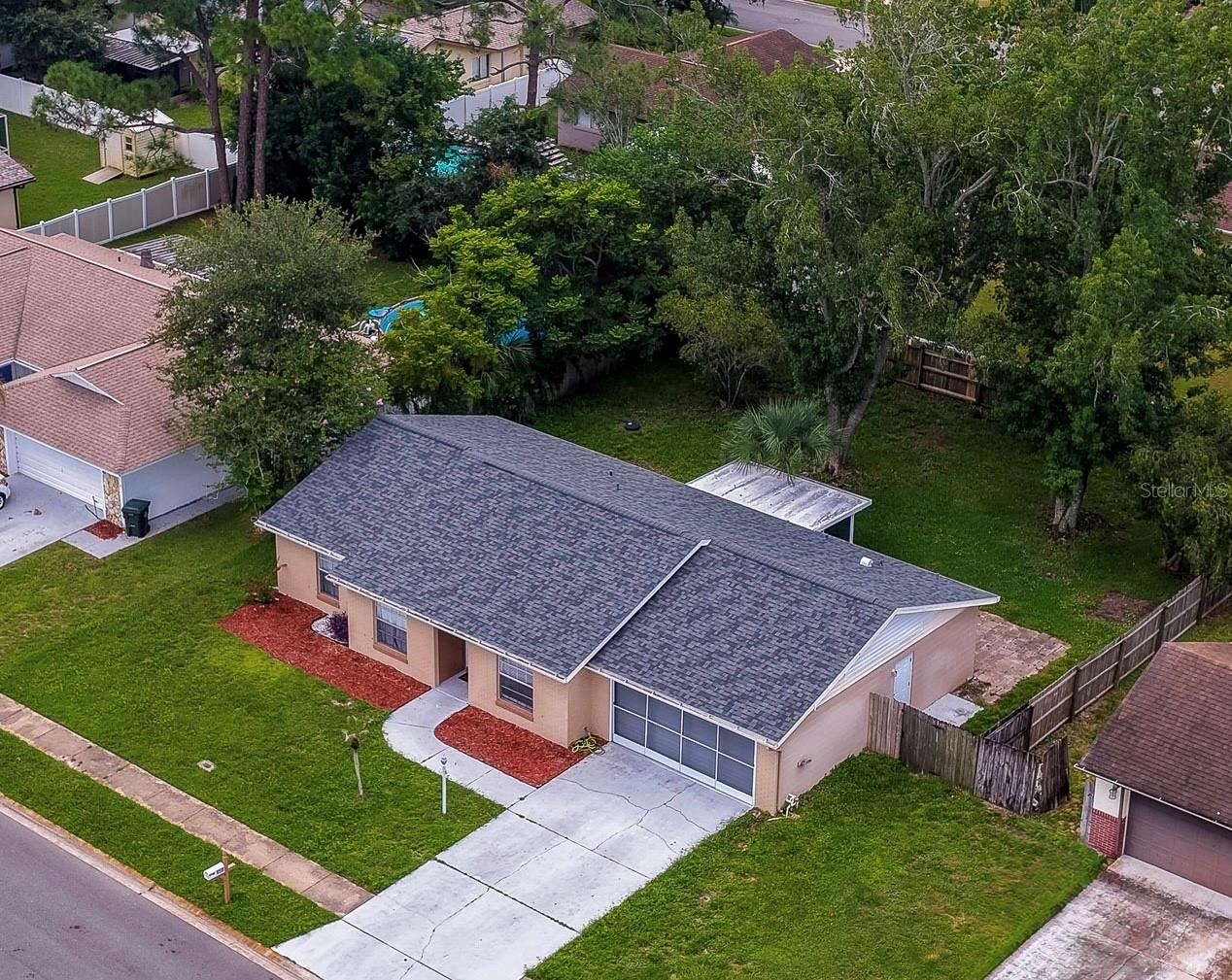 Photo 1 of 20: Elevated perspective of the single-story residence showing a long front walkway, dark roof shingles, and vibrant red mulch landscaping. The property features an expansive front yard bordering a quiet residential street.