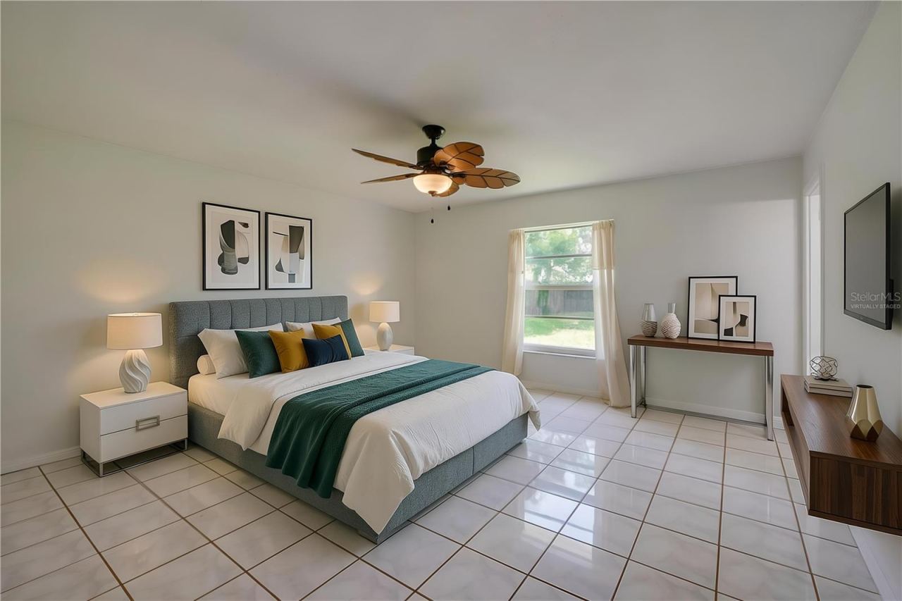 Photo 20 of 20: Virtually Staged. Generous primary bedroom area featuring glossy tiled flooring, neutral walls, and a tropical-style wooden ceiling fan. A single window brings natural light into the open space.