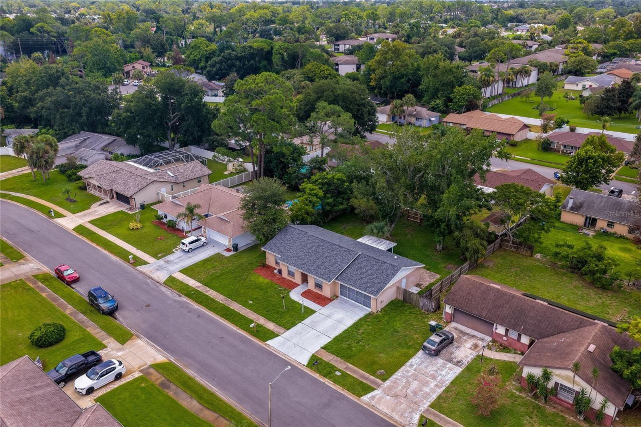 Photo 4 of 20: Aerial view showcasing the property's location within a quiet, tree-lined neighborhood. The single-story home is highlighted alongside its wide driveway, large lot, and surrounding residential community.