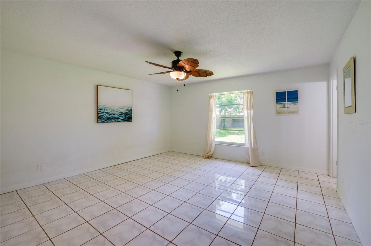 Photo 19 of 20: Generous primary bedroom area featuring glossy tiled flooring, neutral walls, and a tropical-style wooden ceiling fan. A single window brings natural light into the open space.