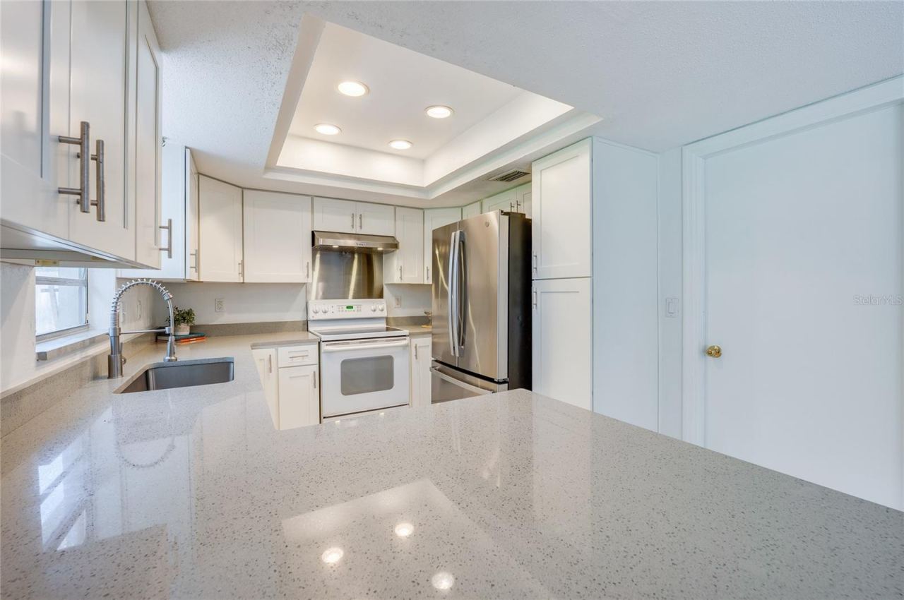 Photo 14 of 20: Bright kitchen layout highlighted by a tray ceiling with inset lighting, ample counter space, and crisp white shaker cabinets. Stainless steel appliances, an undermount sink, and a high-arc faucet offer sleek modern functionality.
