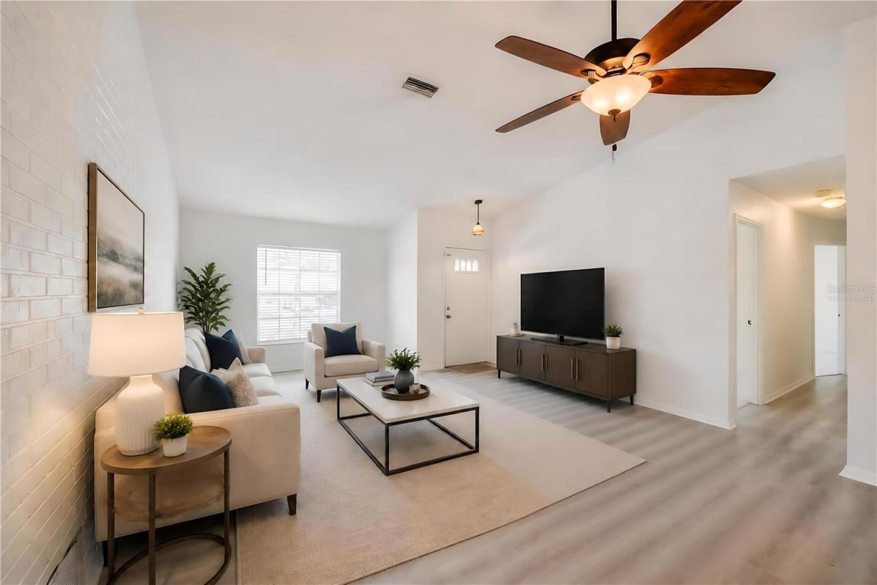 Photo 9 of 20: Virtually Staged. Welcoming foyer and main living room showcasing white walls, modern luxury vinyl flooring, and a ceiling fan with light fixture. A painted brick accent wall adds character to the functional entryway.