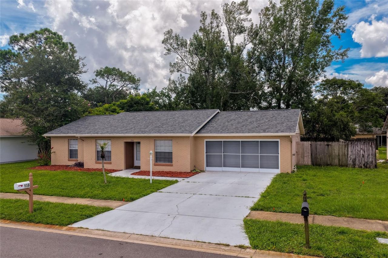 Photo 3 of 20: Front-facing exterior view highlighting a wide concrete driveway, a screened multi-car garage, and a neatly manicured front yard. A wood post mailbox sits near the street curb alongside lush green lawn landscaping.