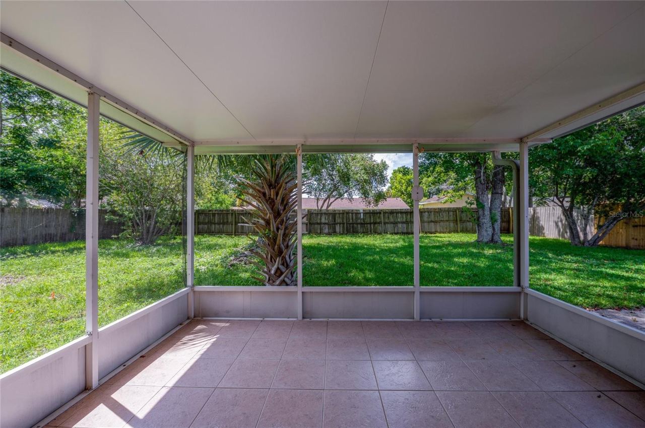 Photo 16 of 20: Enclosed screened porch featuring neutral tile flooring, a solid covered ceiling, and floor-to-ceiling screens overlooking a spacious, grass-covered backyard framed by mature trees and a wooden privacy fence.