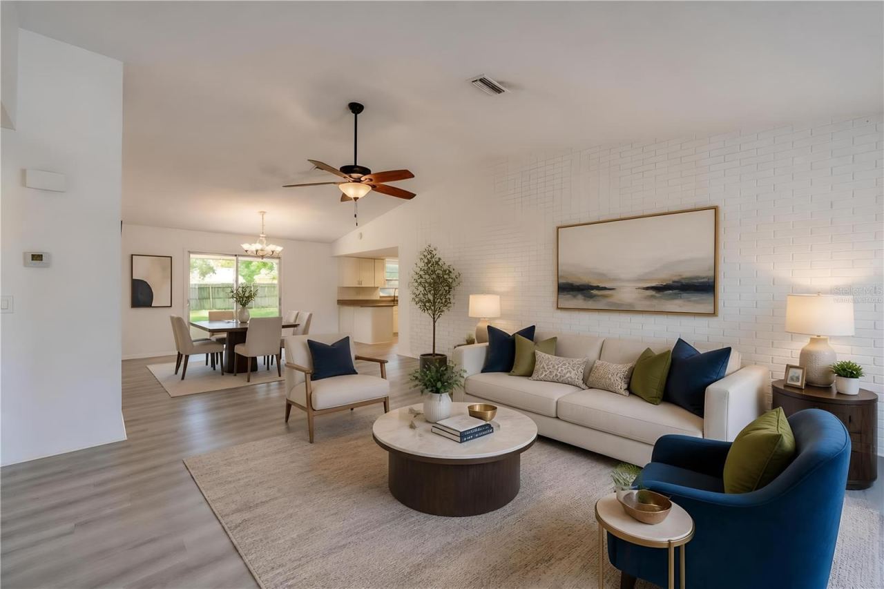 Photo 6 of 20: Virtually Staged. Spacious open-concept living area highlighting light luxury vinyl flooring, a painted white brick accent wall, and a ceiling fan. Sliding glass doors at the rear provide seamless access and views to the backyard patio.