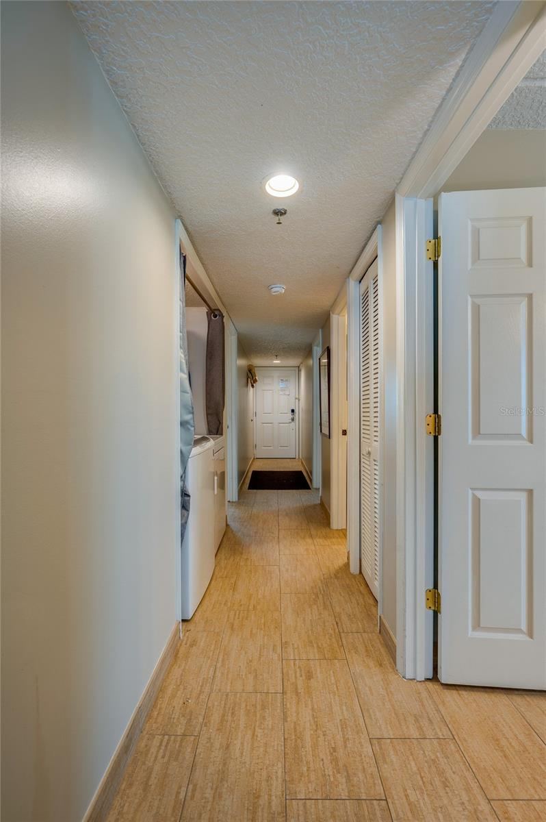 Photo 6 of 20: A well-lit central hallway connects the main living areas with the bedrooms, showcasing consistent tile flooring and a clean, streamlined flow throughout the unit.