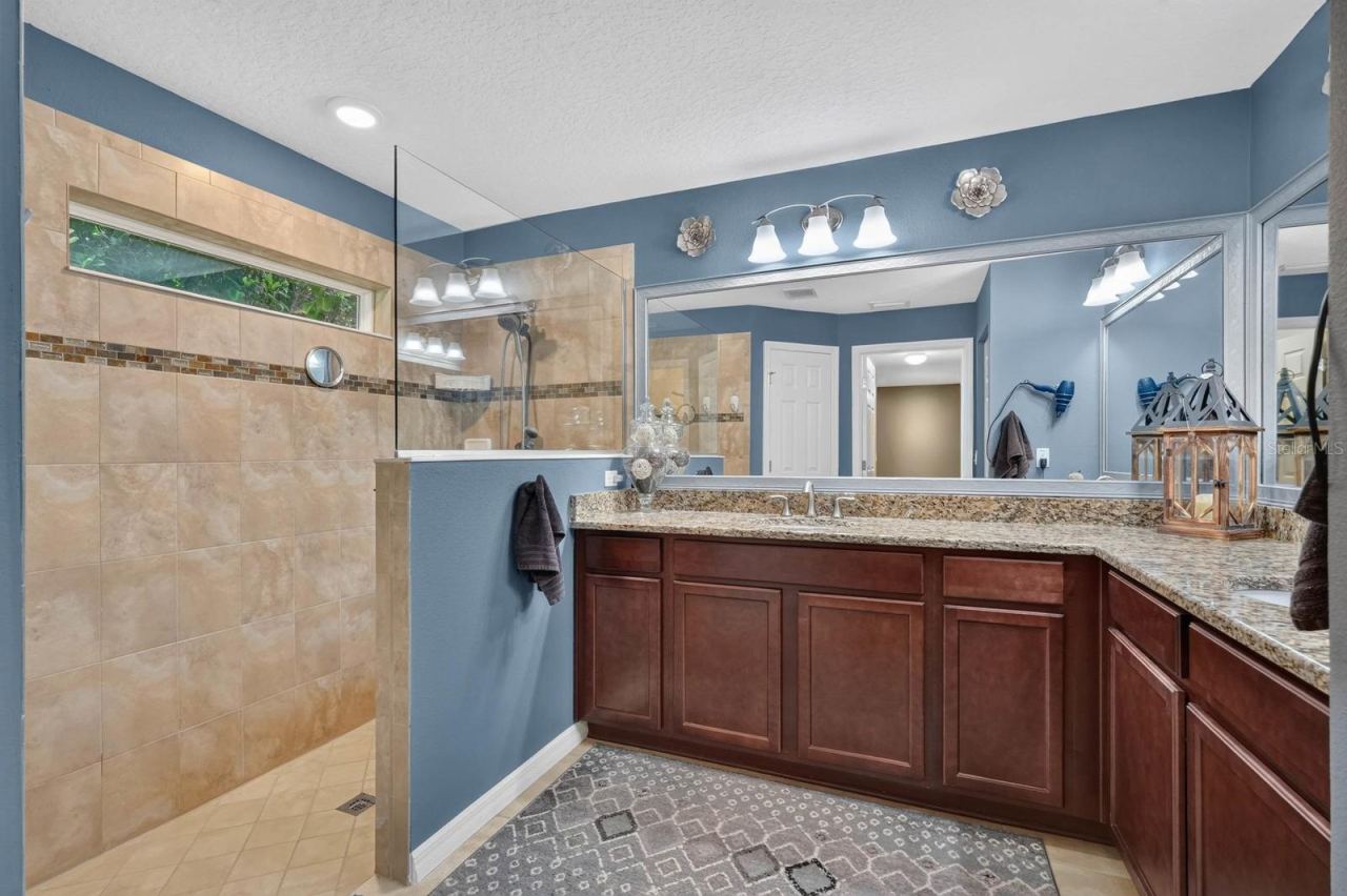 Photo 15 of 20: Primary bathroom features tiled showers, granite countertops, wood cabinetry