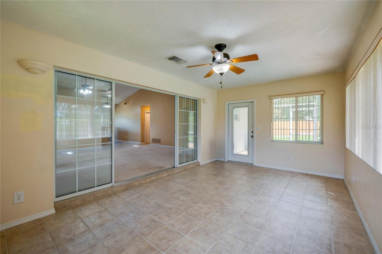 Photo 16 of 20: Versatile sunroom space featuring sliding glass entry doors, tile flooring, a ceiling fan fixture, and a exterior door providing outdoor access.