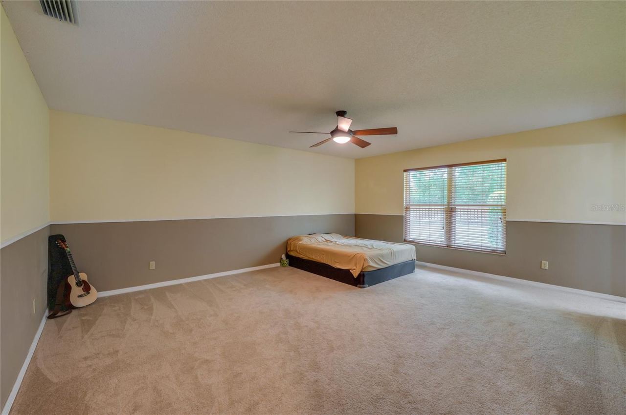 Photo 17 of 20: Spacious primary bedroom featuring soft carpeting, two-tone painted walls, a central ceiling fan, and a large window providing pleasant outdoor views.