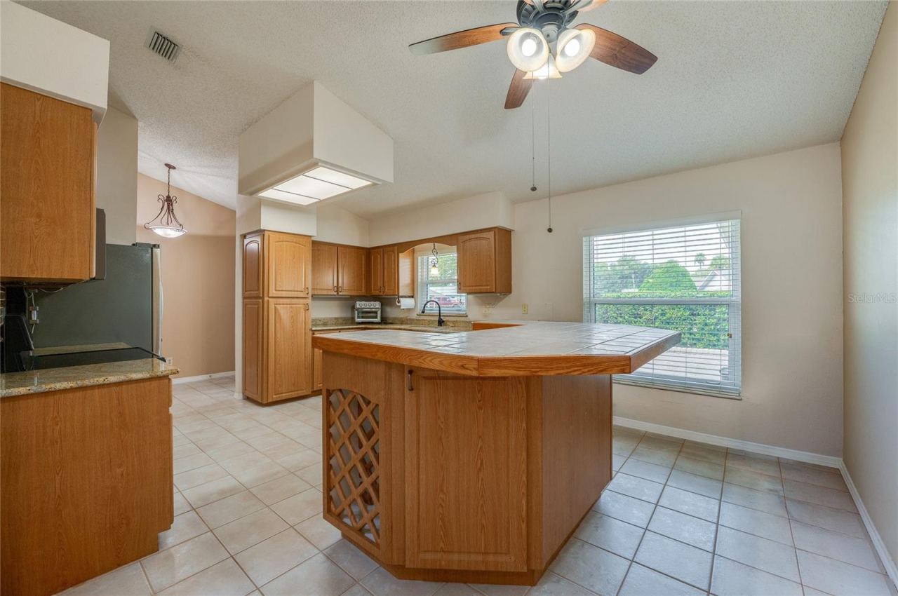 Photo 8 of 20: Spacious kitchen displaying warm wooden cabinetry, a tiled center island with built-in wine storage, tile flooring, and a bright window over the sink.